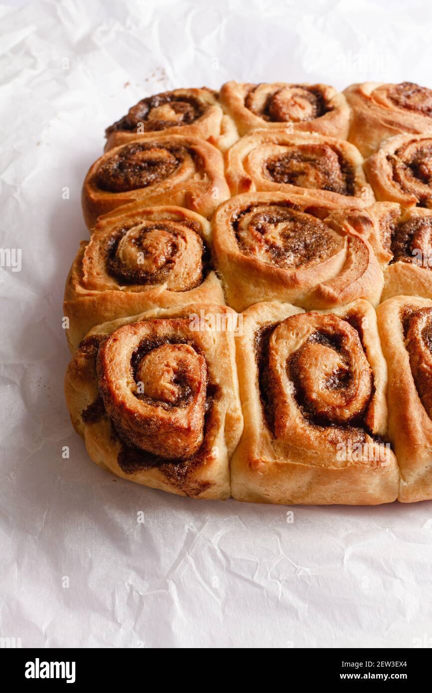 Freshly baked cinnamon rolls still attached together on a piece of white baking paper. Stock Photo