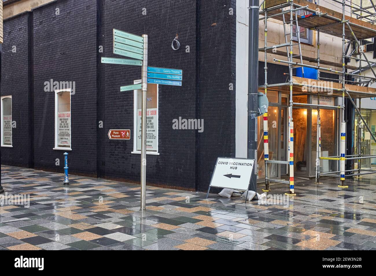 A direction sign for the Covid vaccination hub in the main shopping street of Douglas, Isle of Man on a rainy day Stock Photo