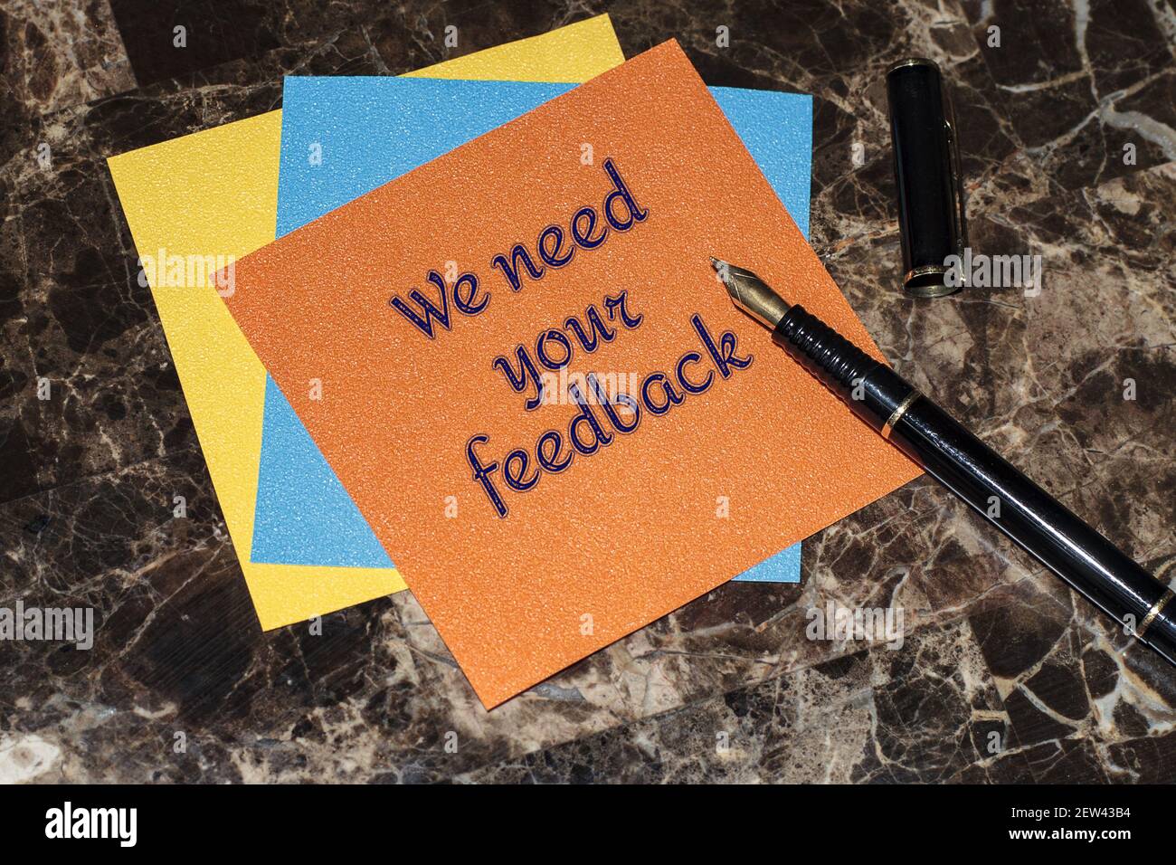 WE NEED YOUR FEEDBACK. Text on a stack of multicolored memo stickers