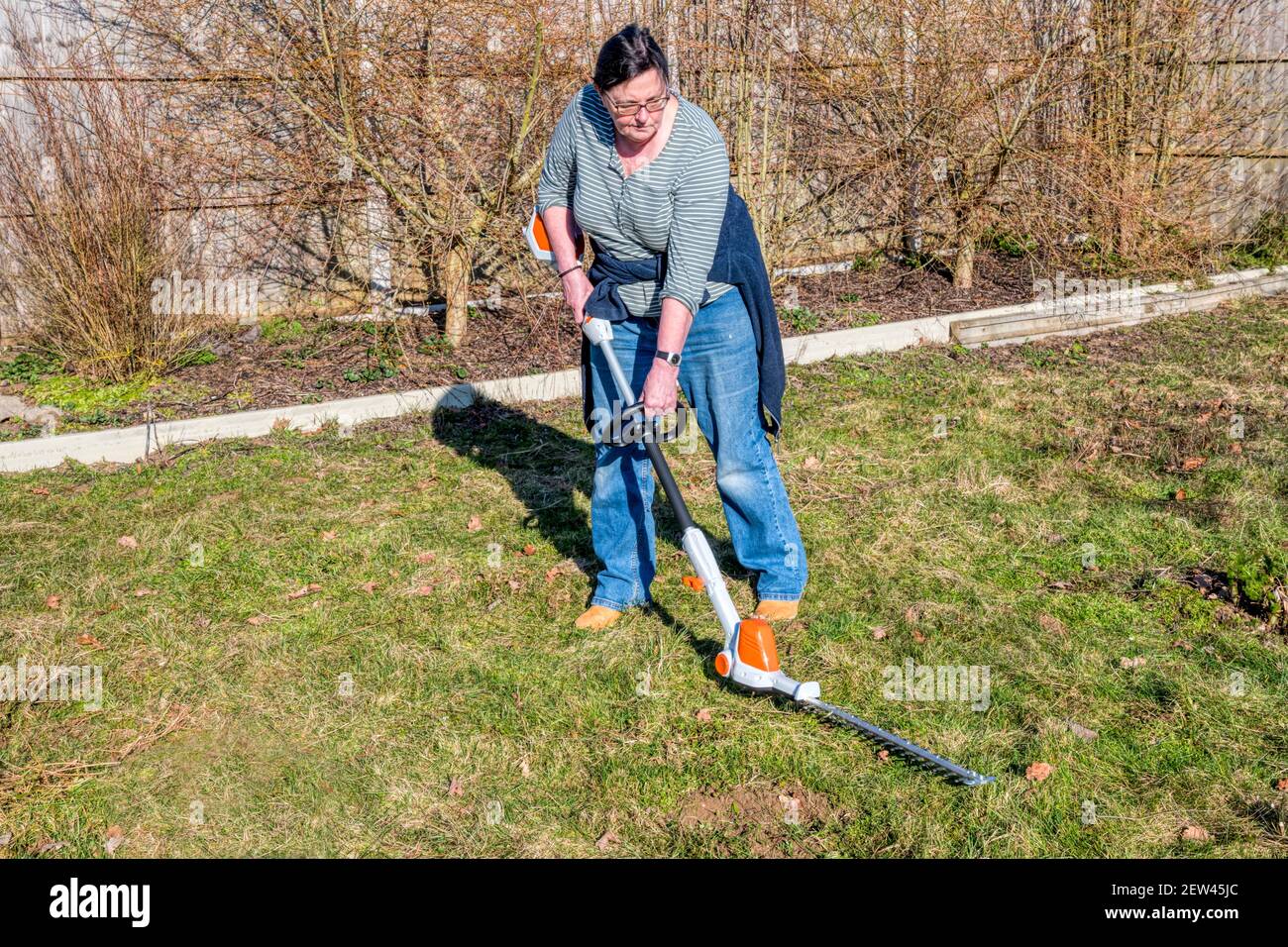 Woman clearing area of rough grassland or meadow using a hedge trimmer. Stock Photo