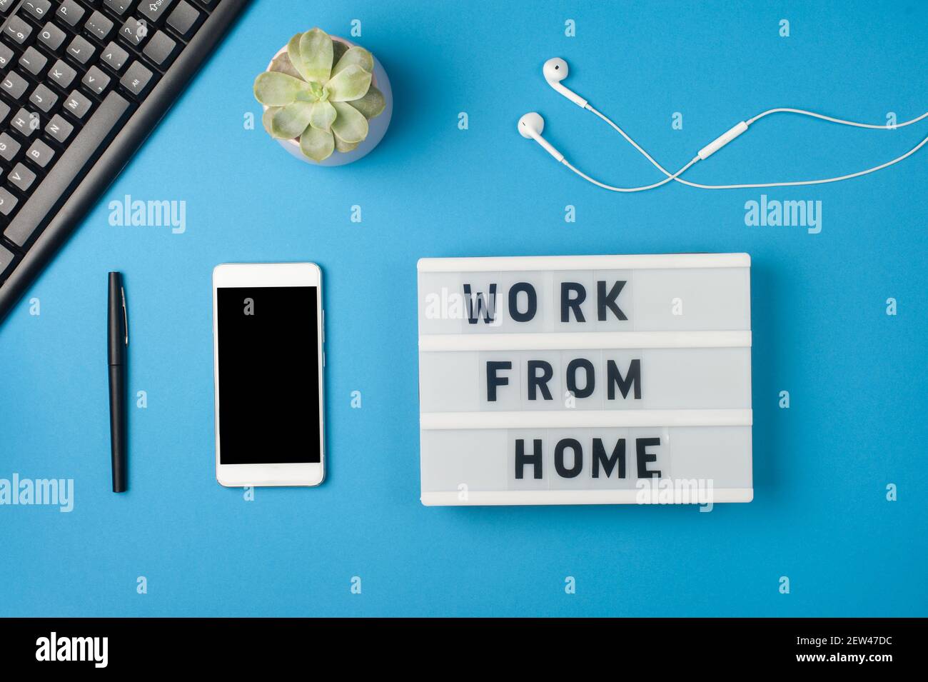 Work from home - text on display lightbox and smartphone mockup on blue background workplace. Black keyboard and white earphones. Freelance work conce Stock Photo