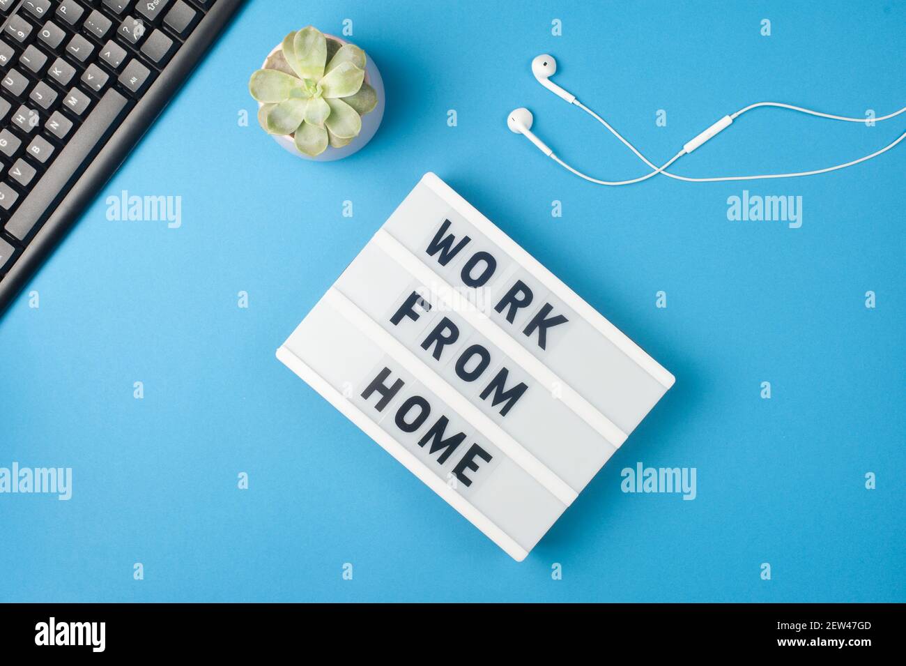 Work from home - text on display lightbox on blue background workplace. Black keyboard and white earphones. Freelance work concept Stock Photo