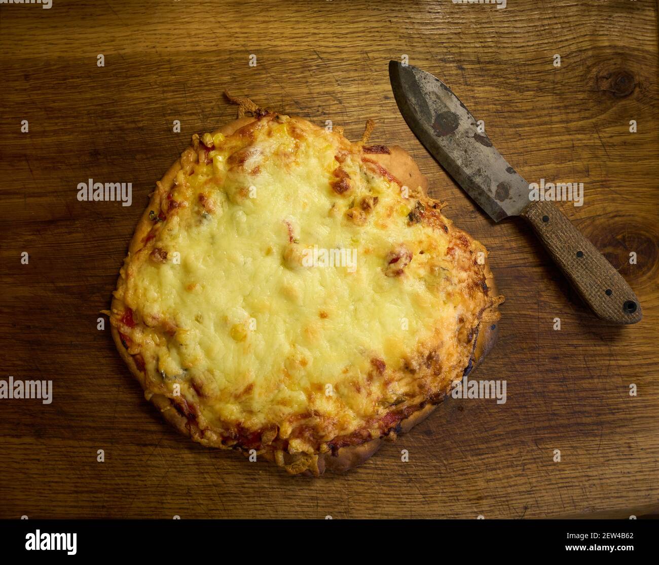 Home cooked flatbread cheese and tomato pizza on a wooden board next to a rustic carbon steel knife with patina on blade Stock Photo