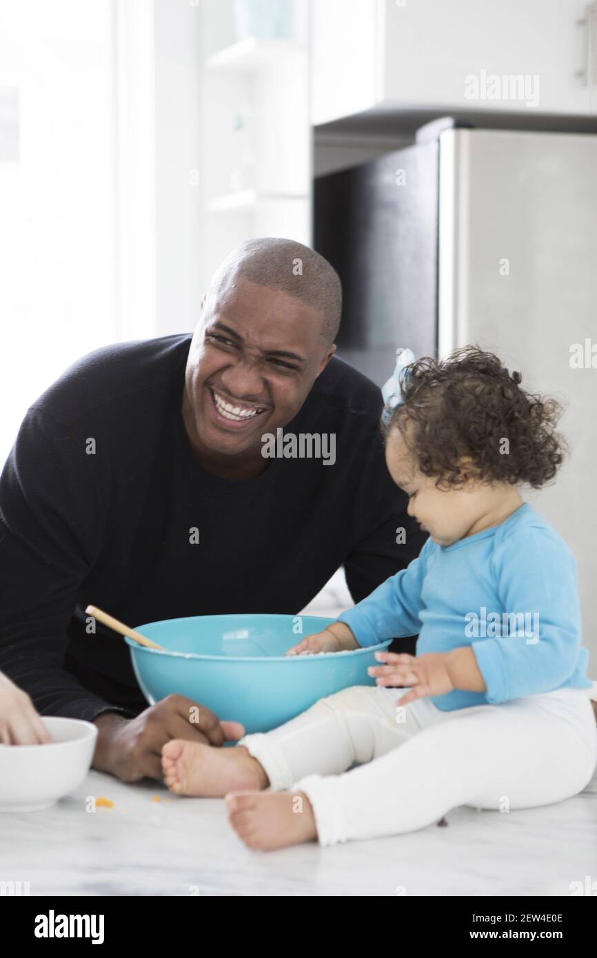 A Dad laughs as he spends time in the kitchen with his daughter. They are baking, Stock Photo
