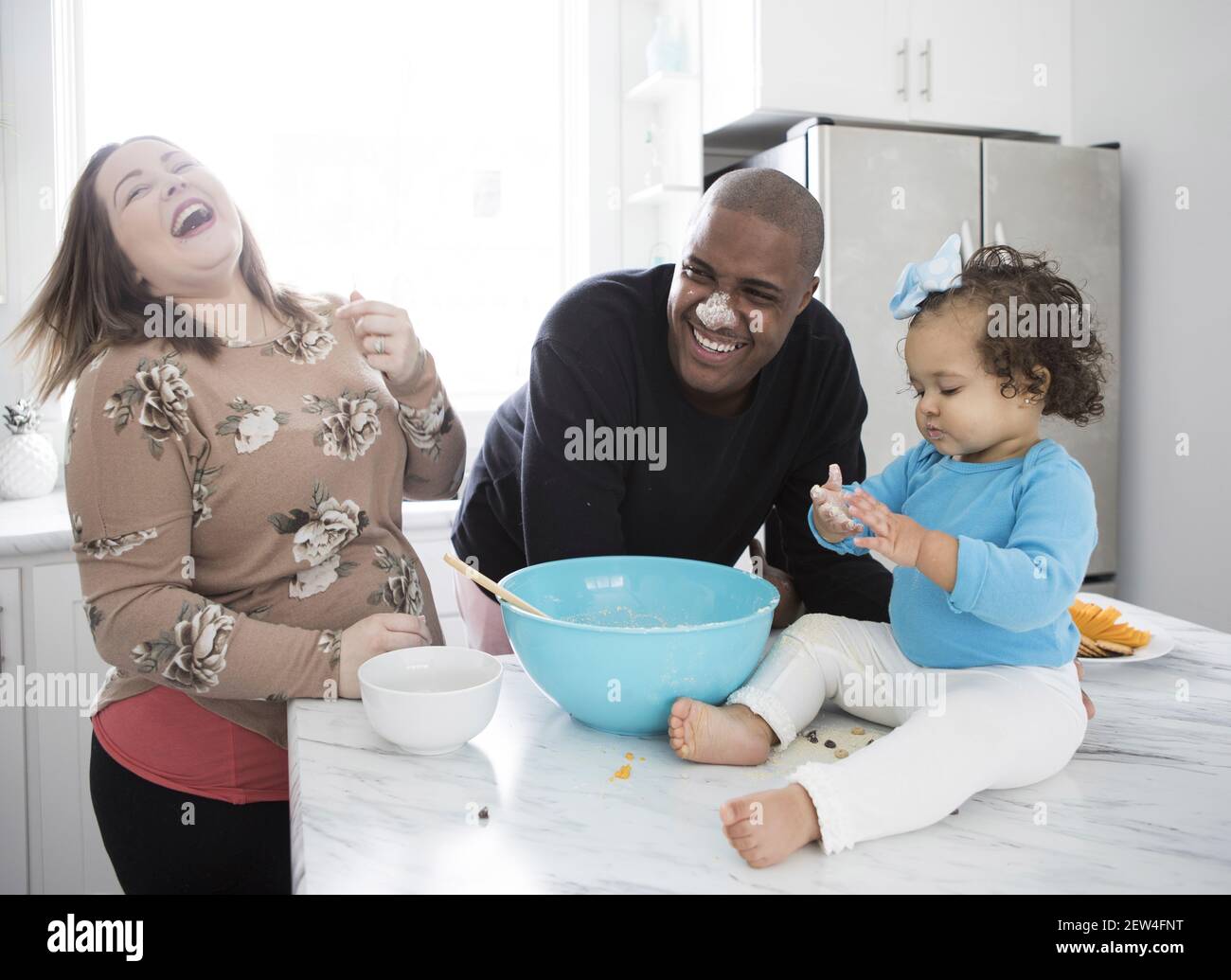 A young interracial family cooking and laughing together in a modern kitchen. Stock Photo
