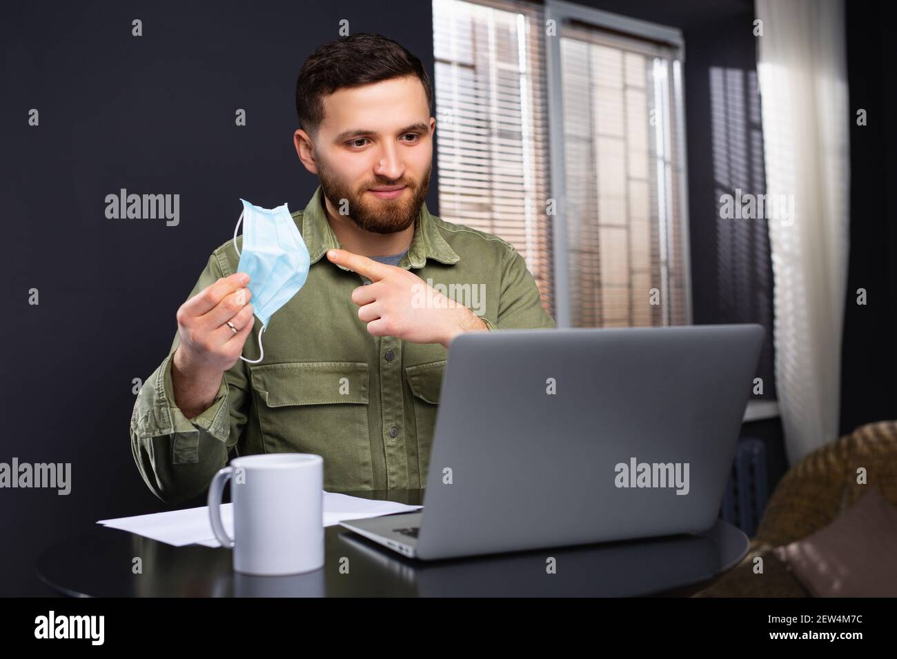 A man during a conference points at the camera with a medical mask pointing at it with his index finger. Calling for stringent safeguards against the Stock Photo