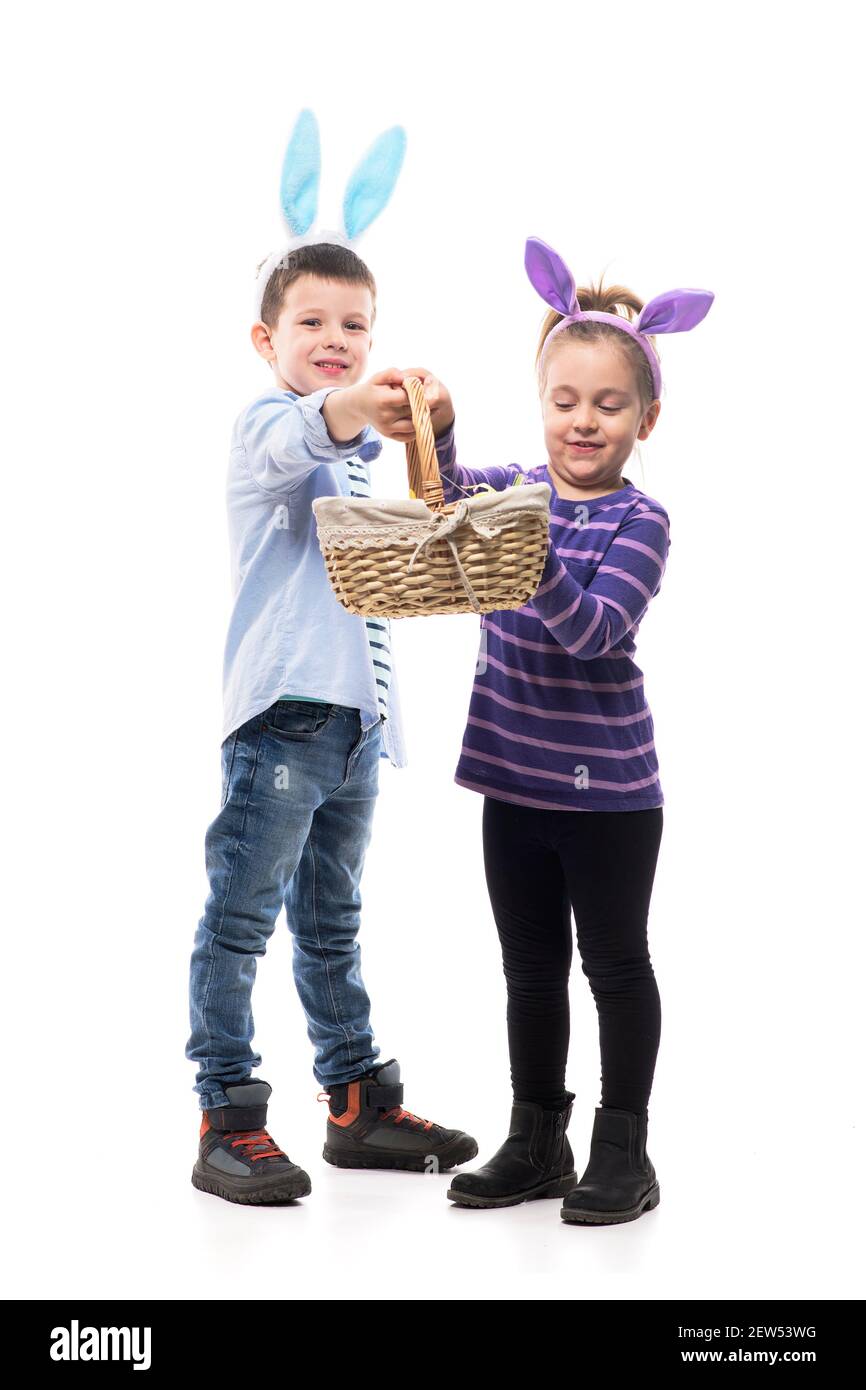 Happy playful boy and little girl with bunny ears showing and holding basket with Easter eggs. Full body isolated on white background. Stock Photo