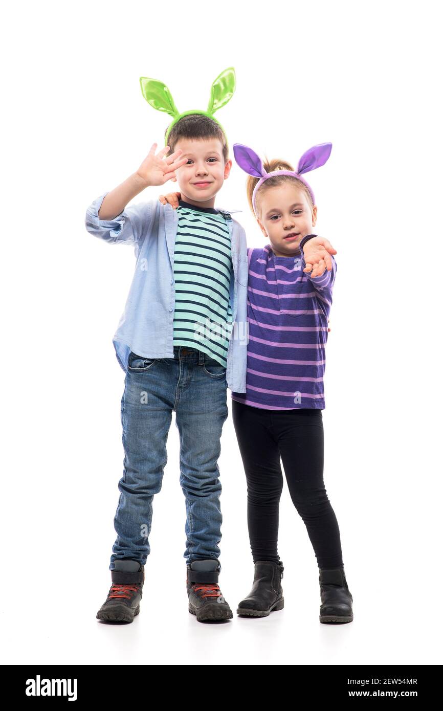 Hugged young brother and sister with Easter bunny ears greeting and waving at camera. Full body isolated on white background. Stock Photo