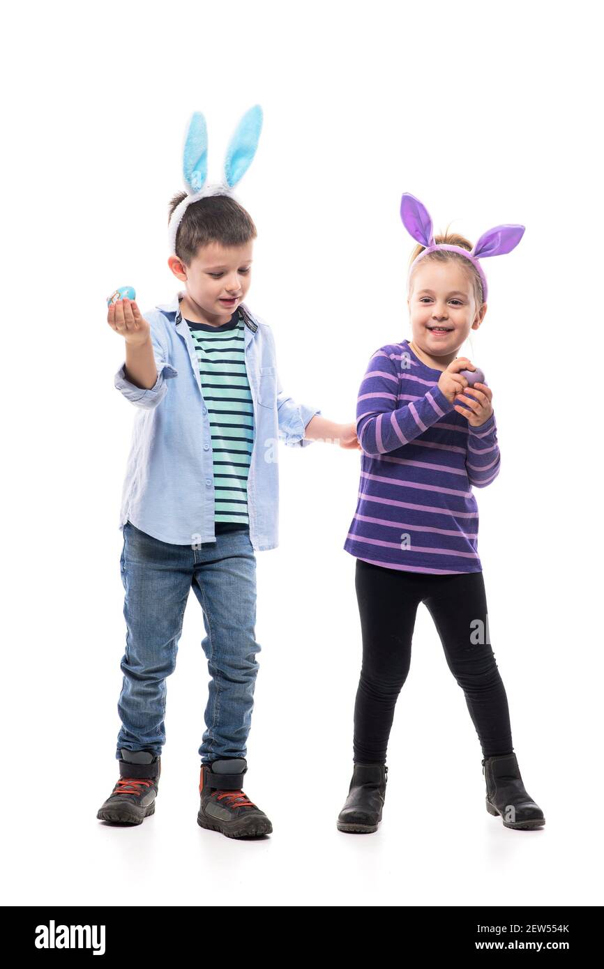 Cute playful little boy and toddler girl with Easter bunny ears playing egg tapping game. Full