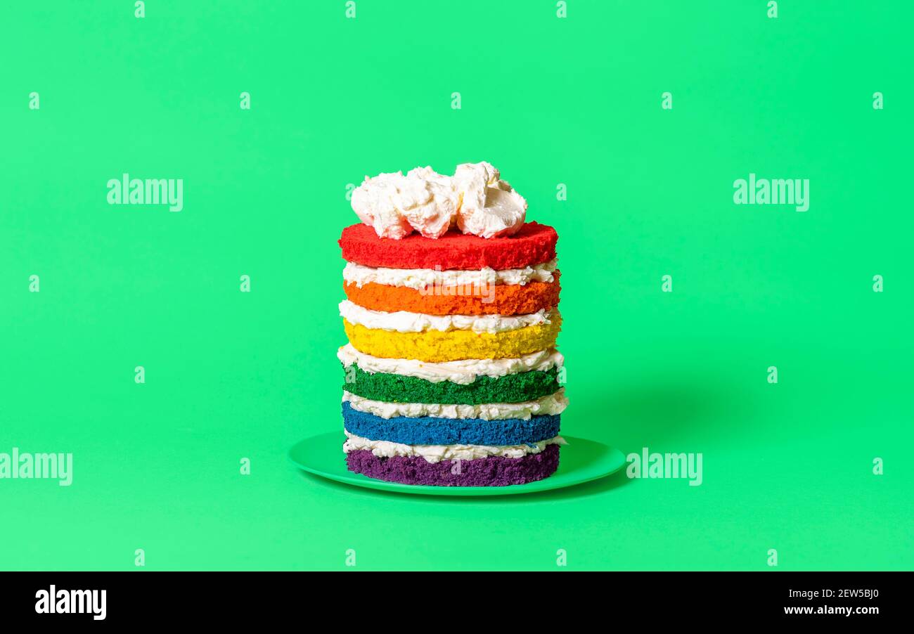 Birthday cake with six colored layers and whipped cream. Rainbow cake side view against a green background. Stock Photo
