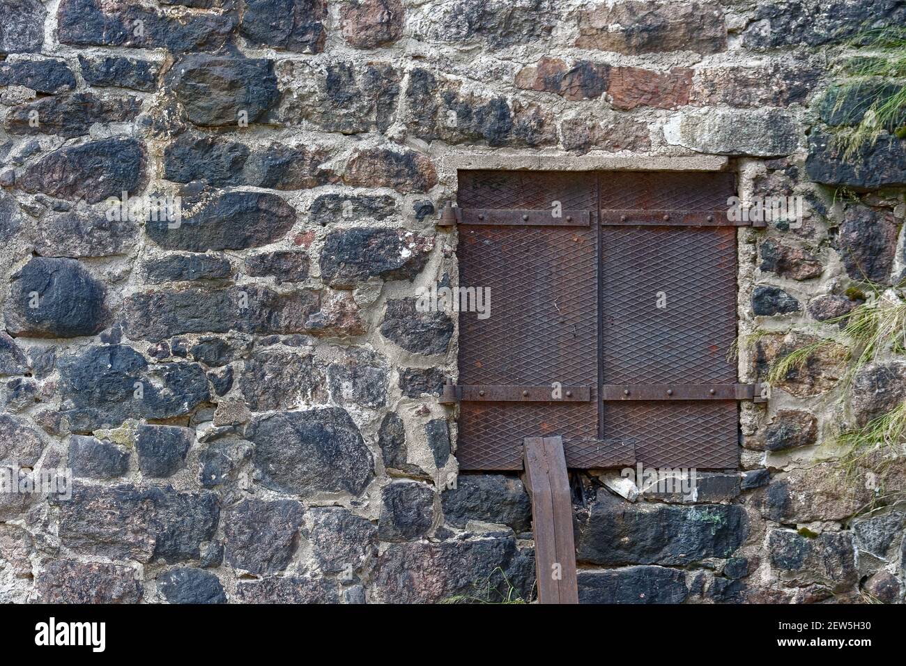 Rectangular window closed with reinforced iron sheet shutters on the stone wall of the old town hall. From the window of the world series. Stock Photo