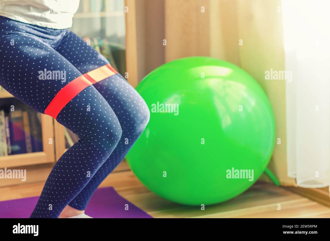 Attractive sporty woman wearing green top and gray leggings standing near  green background holding pink dumbbells and smiling. Stock Photo