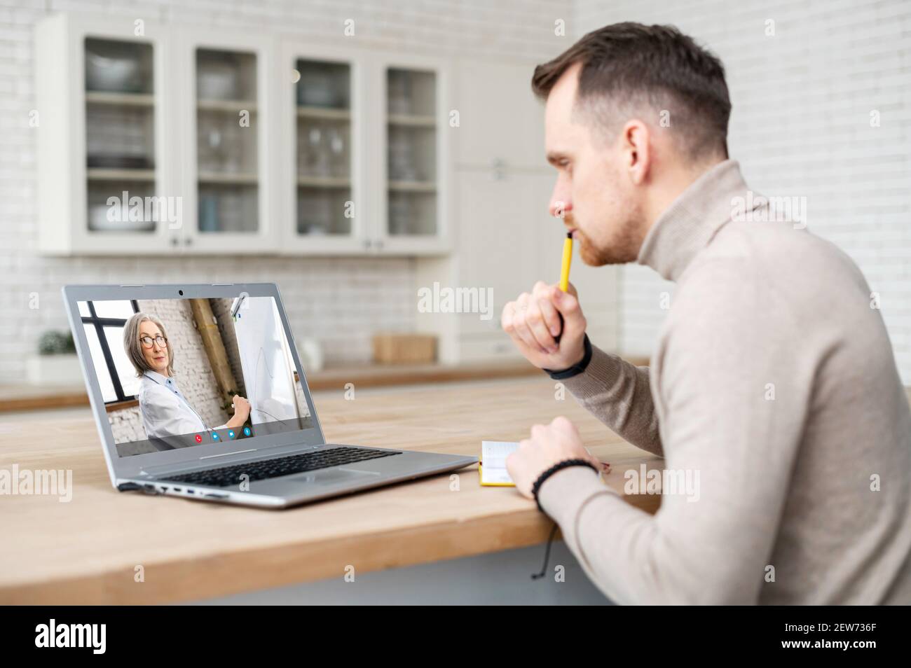 Mature adult student with pen in the hand and notebook, sitting at home at the laptop on a business course, listening to the senior female speaker who showing and explaining in a graph, concentrated Stock Photo
