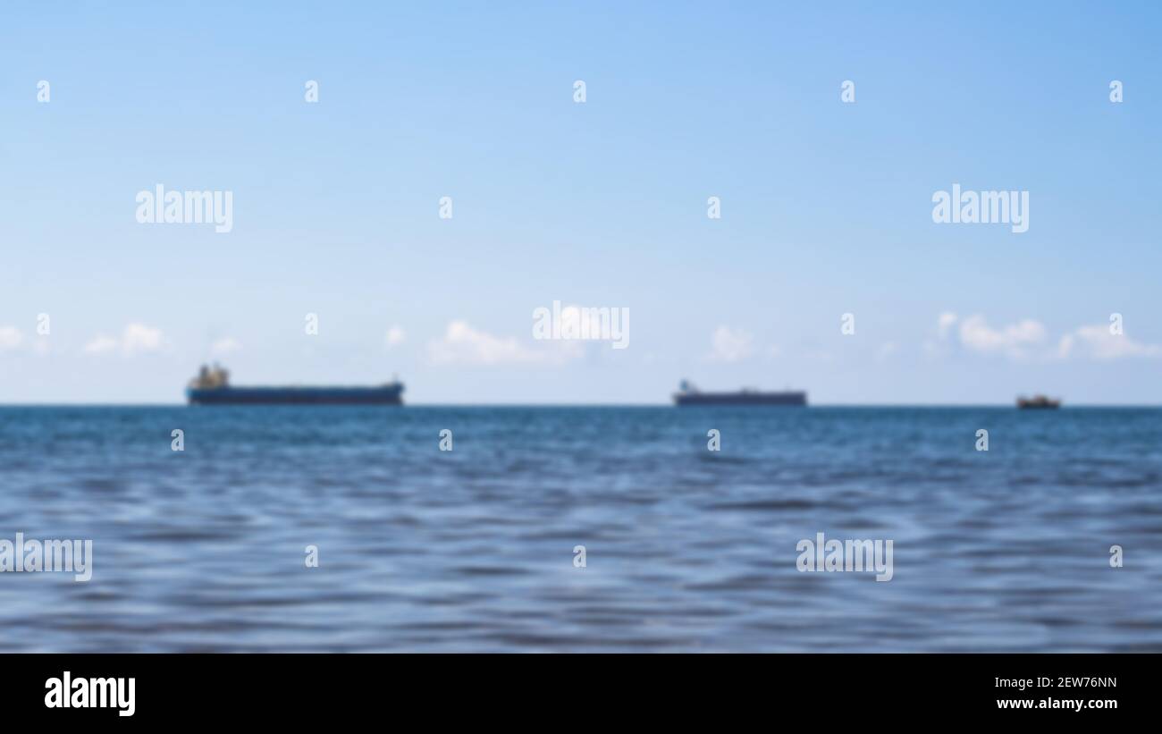 Defocused close-up of a minimalistic seascape on a bright summer day. Blue sea, clouds over the horizon, and several cargo ships. Stock Photo