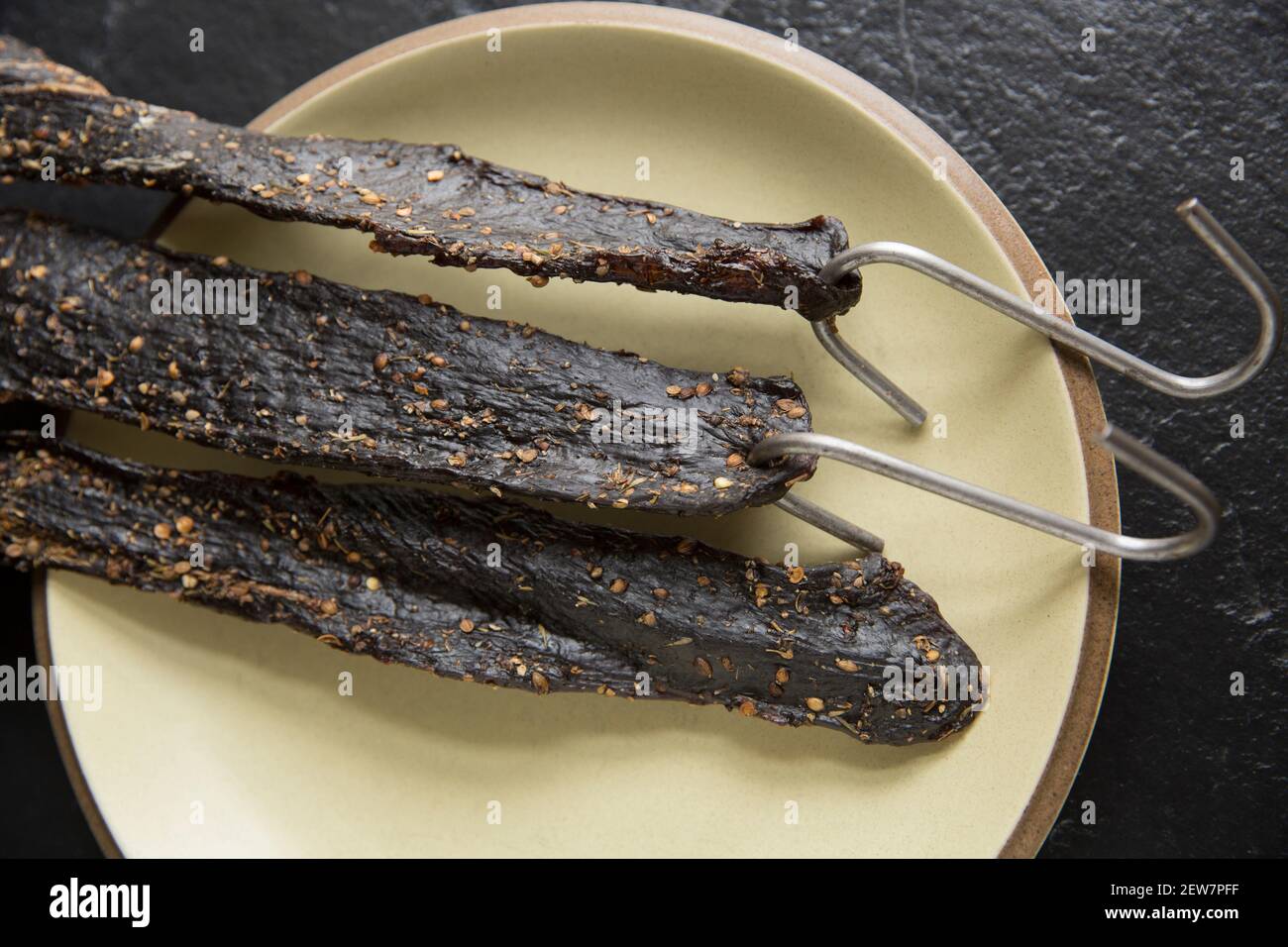 Venison from a wild fallow deer that has been hung on hooks to air dry to make homemade biltong. It was cured with salt, brown sugar and malt vinegar Stock Photo