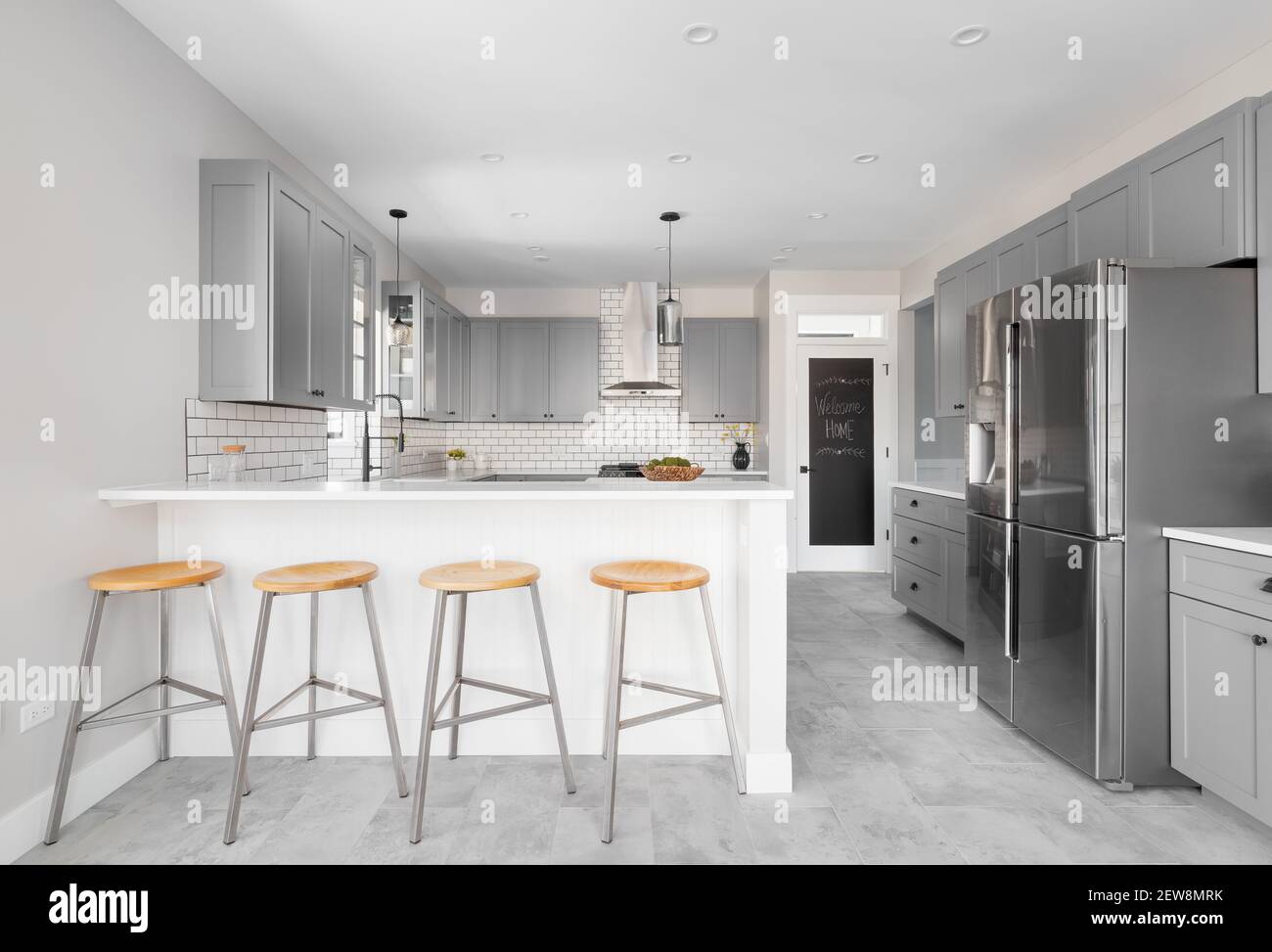 A grey kitchen with stainless steel appliances grey tile flooring a white subway tile backsplash and bar stools sitting at the countertop Stock Photo Alamy