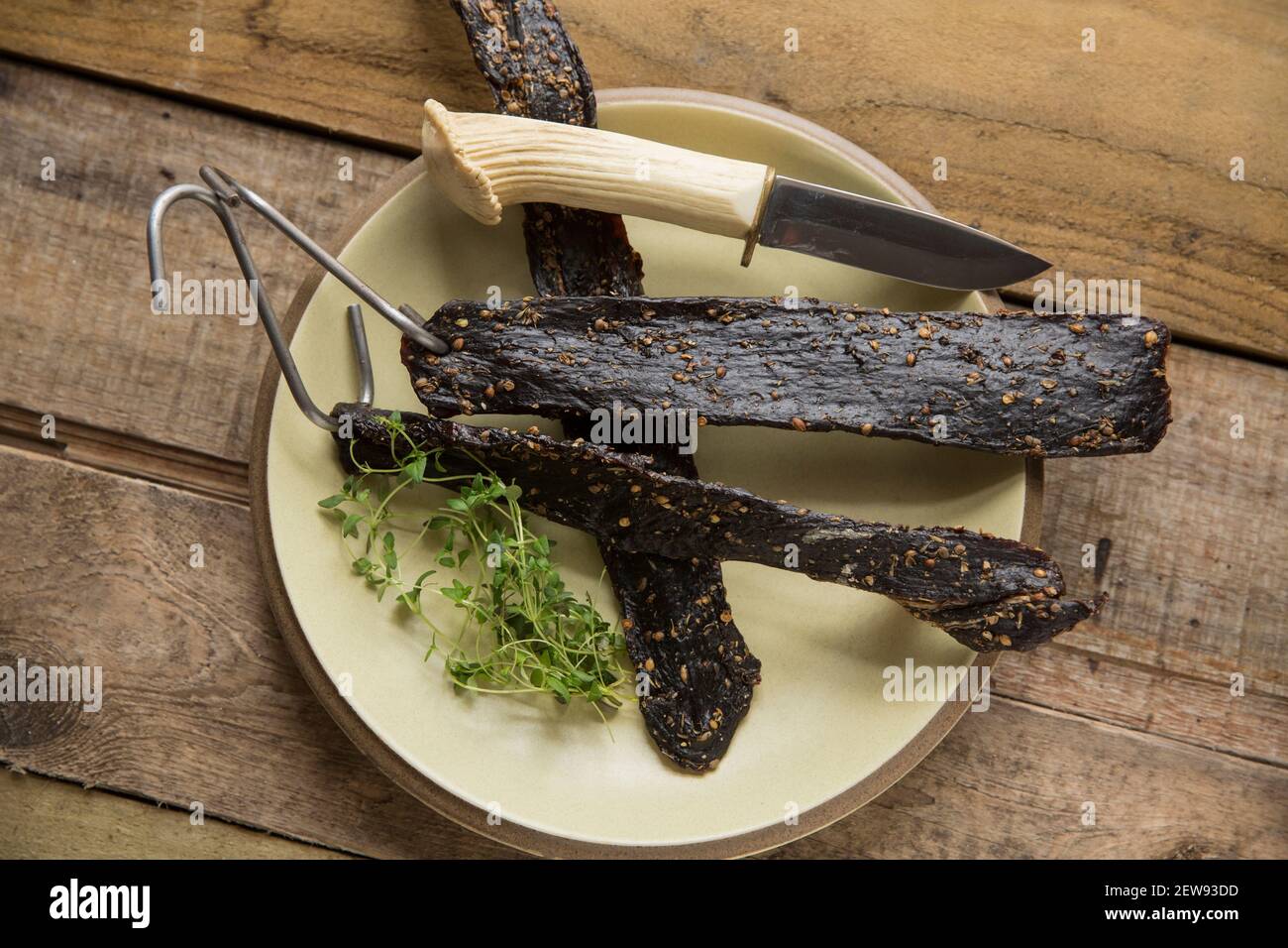 Venison from a wild fallow deer that has been hung on hooks to air dry to make homemade biltong. It was cured with salt, brown sugar and malt vinegar Stock Photo