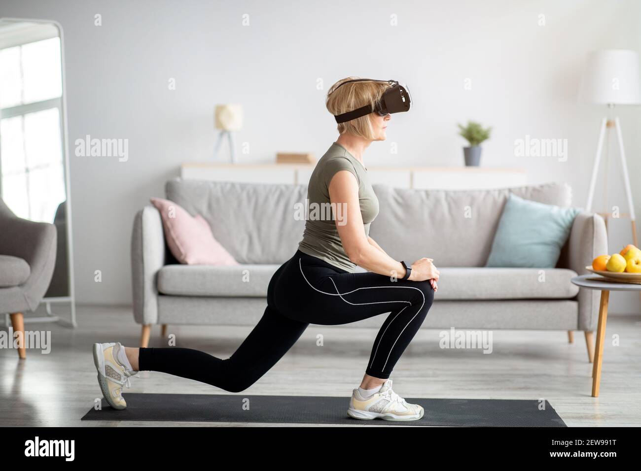 Virtual workout. Side view of senior lady in VR glasses doing lunges at ...