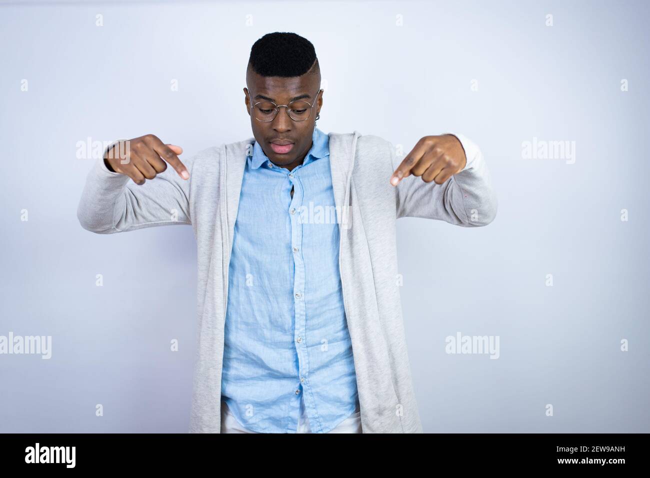 Young handsome african american man wearing casual clothes surprised, looking down and pointing down with fingers and raised arms Stock Photo