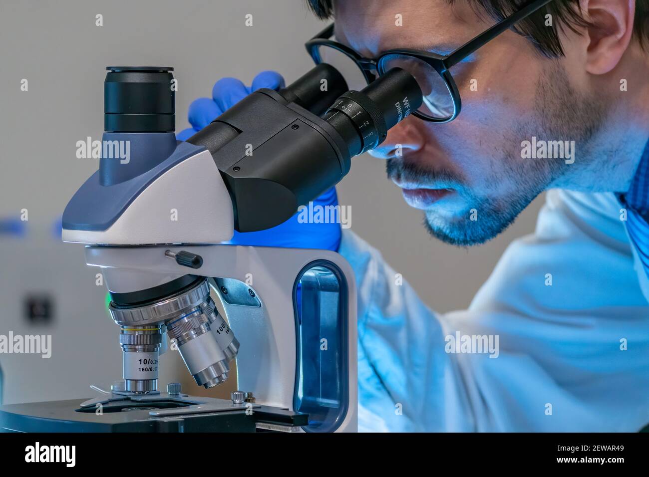 Young scientist in laboratory is looking inside microscope. Stock Photo
