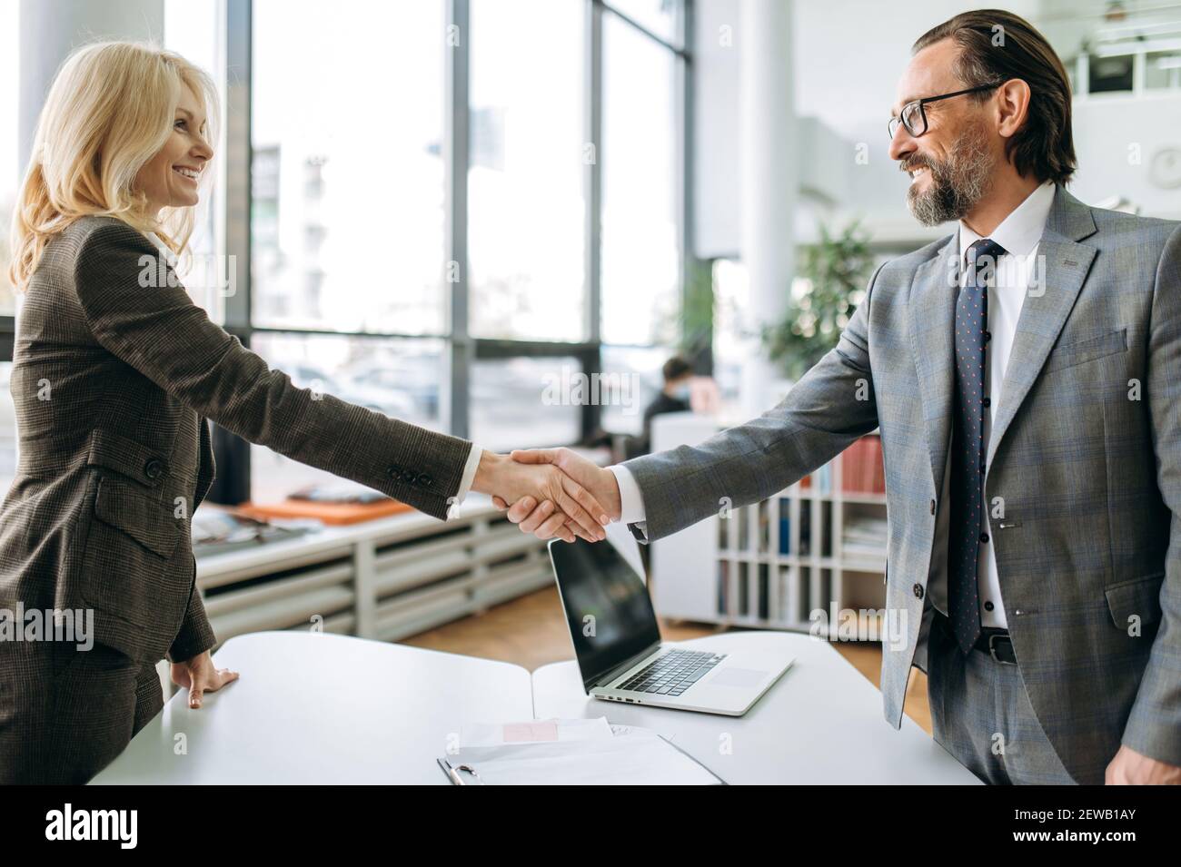 Confident influential coworkers shaking hands on business meeting, starting negotiations. Successful middle aged colleagues coming to agreement, sign an important contract Stock Photo