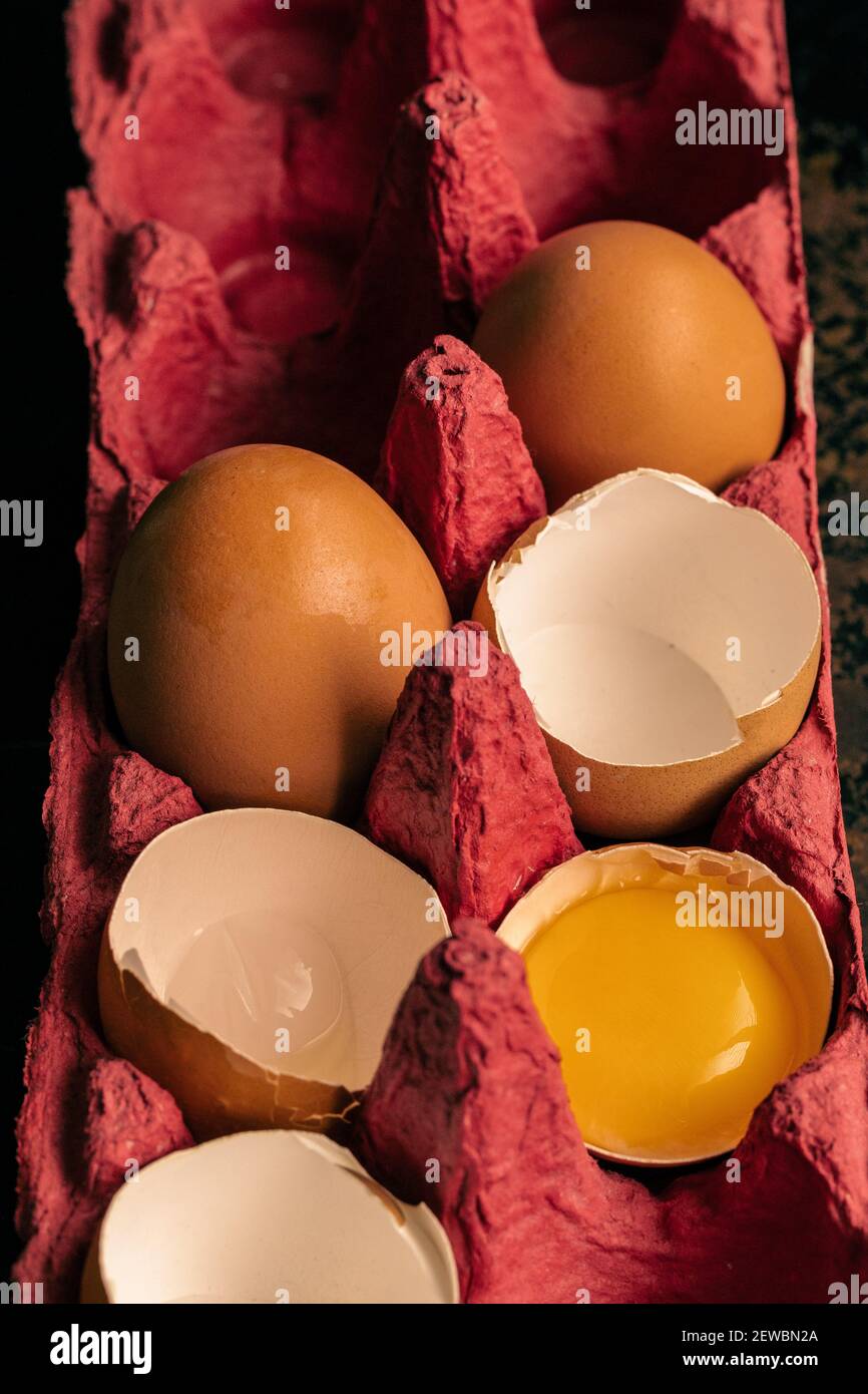 broken eggs in a red egg crate; one egg yolk in the shell Stock Photo