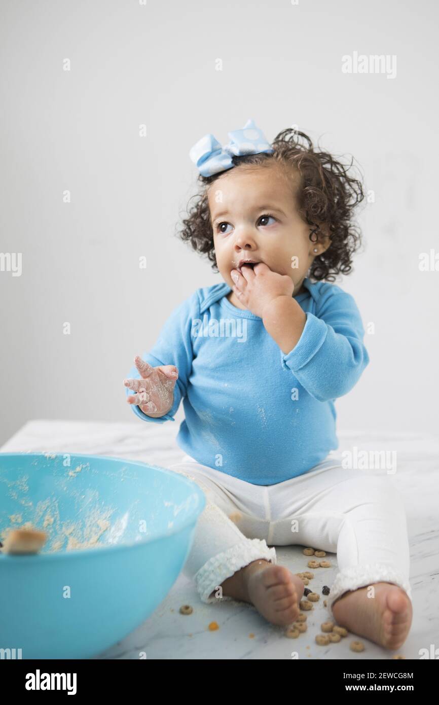 A little girl sitting on a counter making a mess with  baking ingredients. Stock Photo