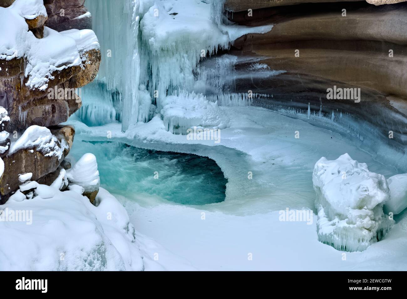 A horizontal image of The Athabasca falls in winter with frozen icicles clinging to the rock canyon walls in Jasper National Park in Alberta Canada. Stock Photo