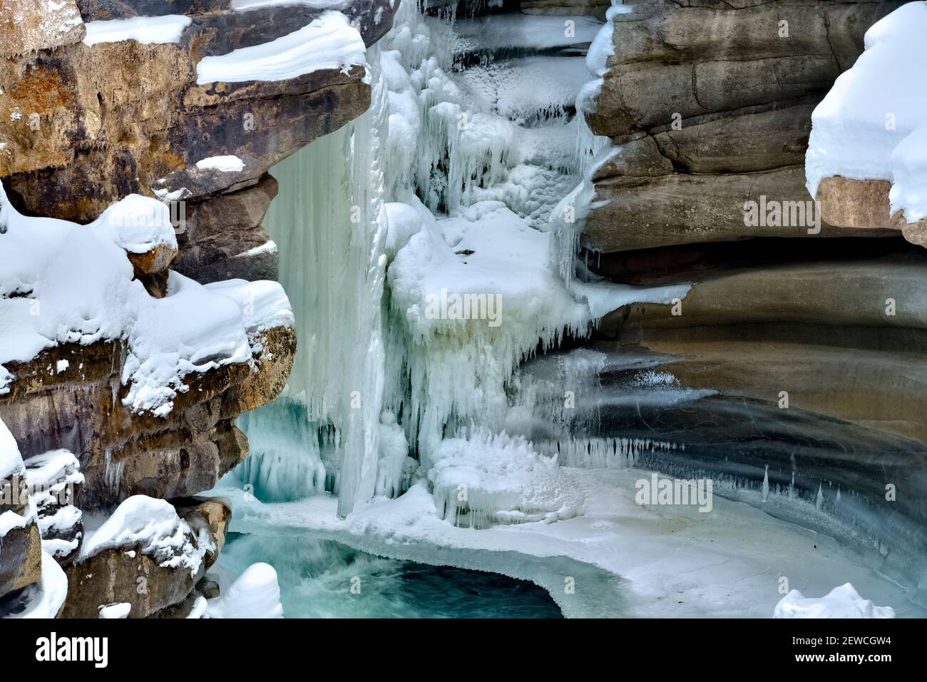 A horizontal image of The Athabasca falls in winter with frozen ice clinging to the rock canyon walls in Jasper National Park in Alberta Canada. Stock Photo