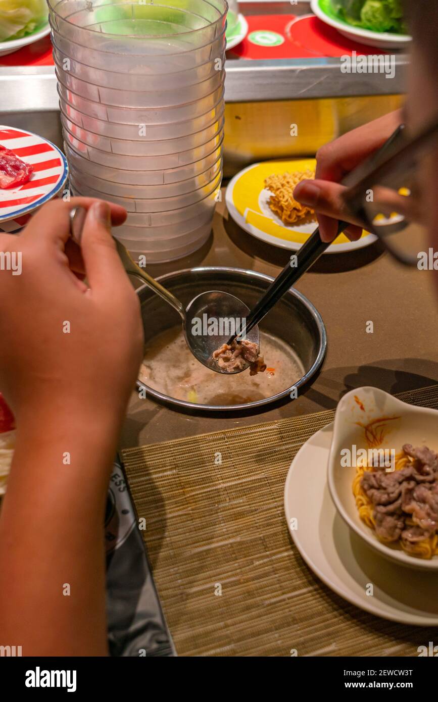Close up photo of woman eating at conveyor belt hotpot restaurant Stock
