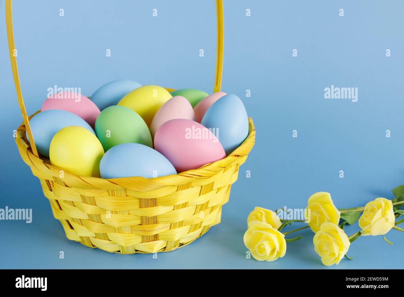 Easter eggs in basket with small flowers aside and copy space on blue background. Easter composition. Stock Photo