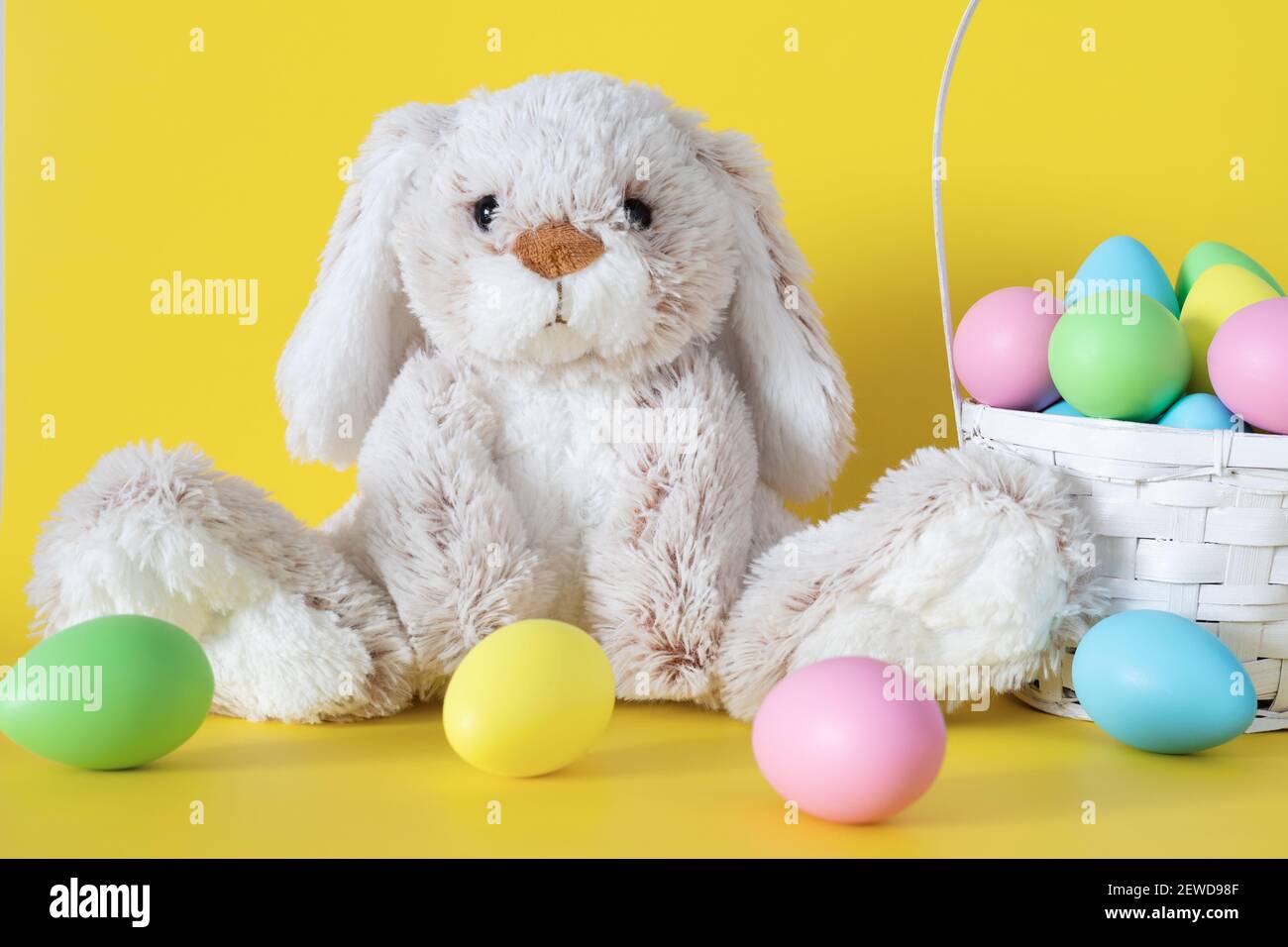 Easter stuffed bunny with colored eggs and easter basket on yellow background Stock Photo