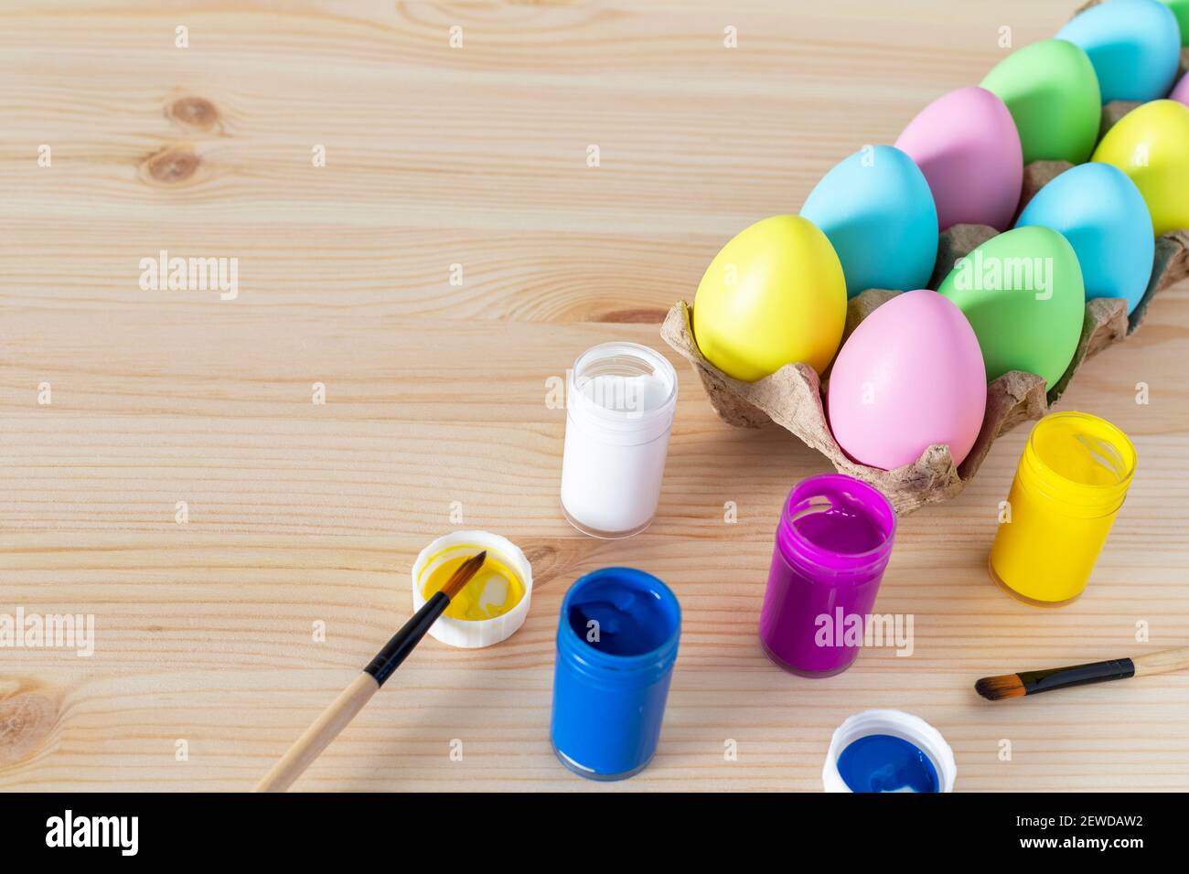 Easter eggs and colored paints with paintbrushes on the table. Easter craft concept. Stock Photo