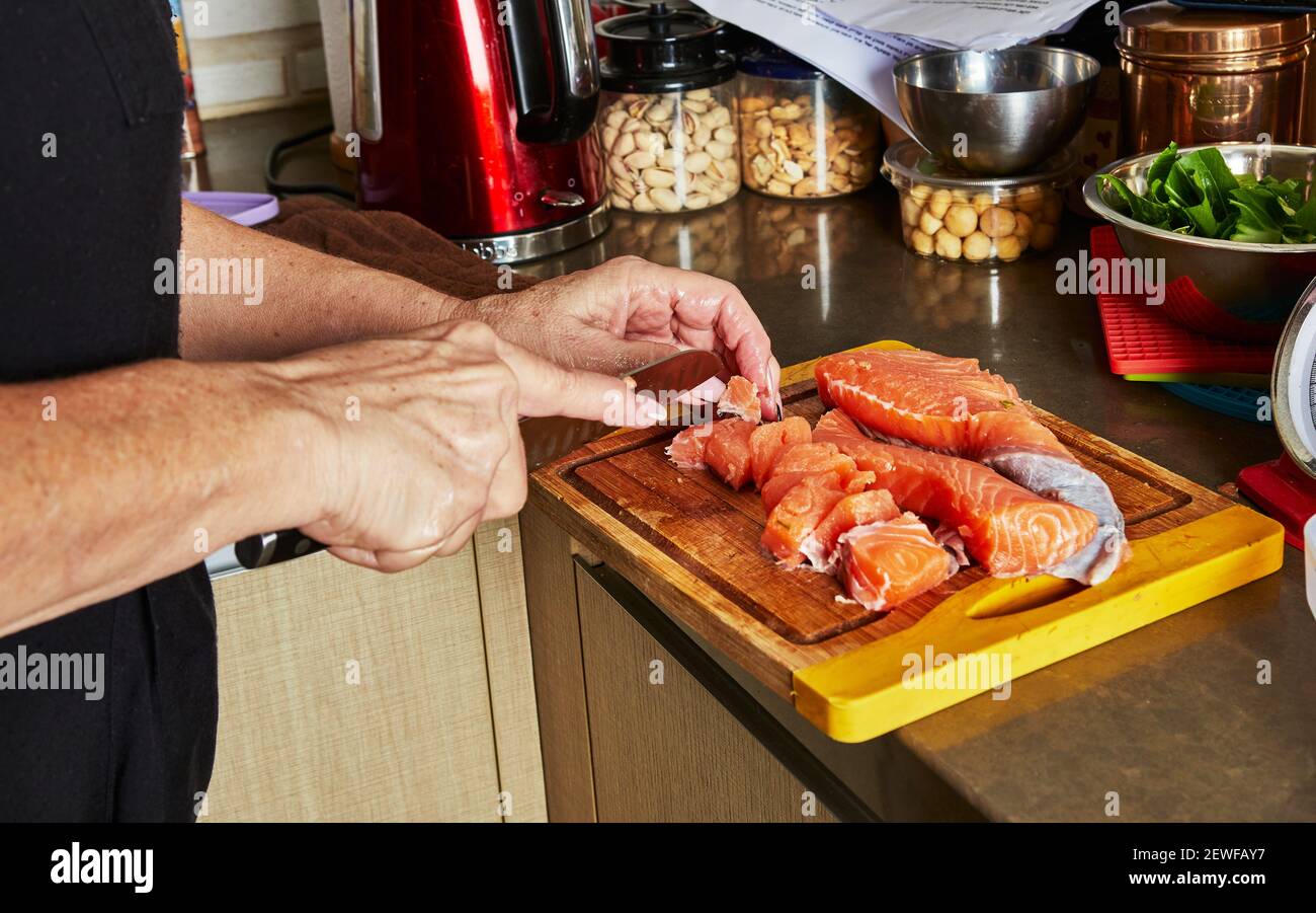 Cooking at home in the kitchen according to recipe from the Internet. Woman cuts fresh salmon with knife on cutting board. Step by step recipe Stock Photo