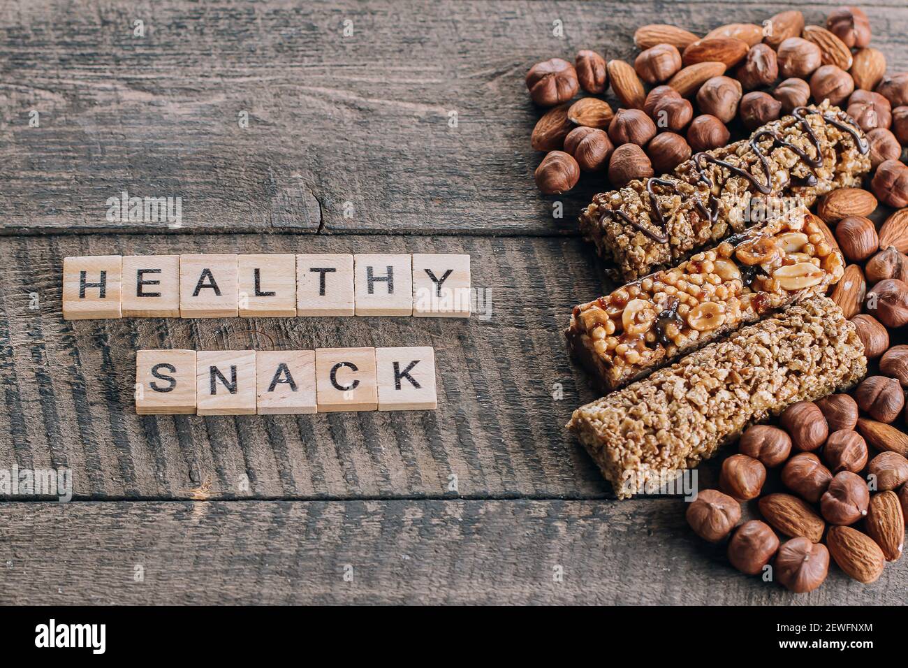 Cereal Granola bars and almond, hazelnut nuts. Old Brown Wooden Table Background. Wooden letters words text Healthy Snack Bars. Top view Stock Photo