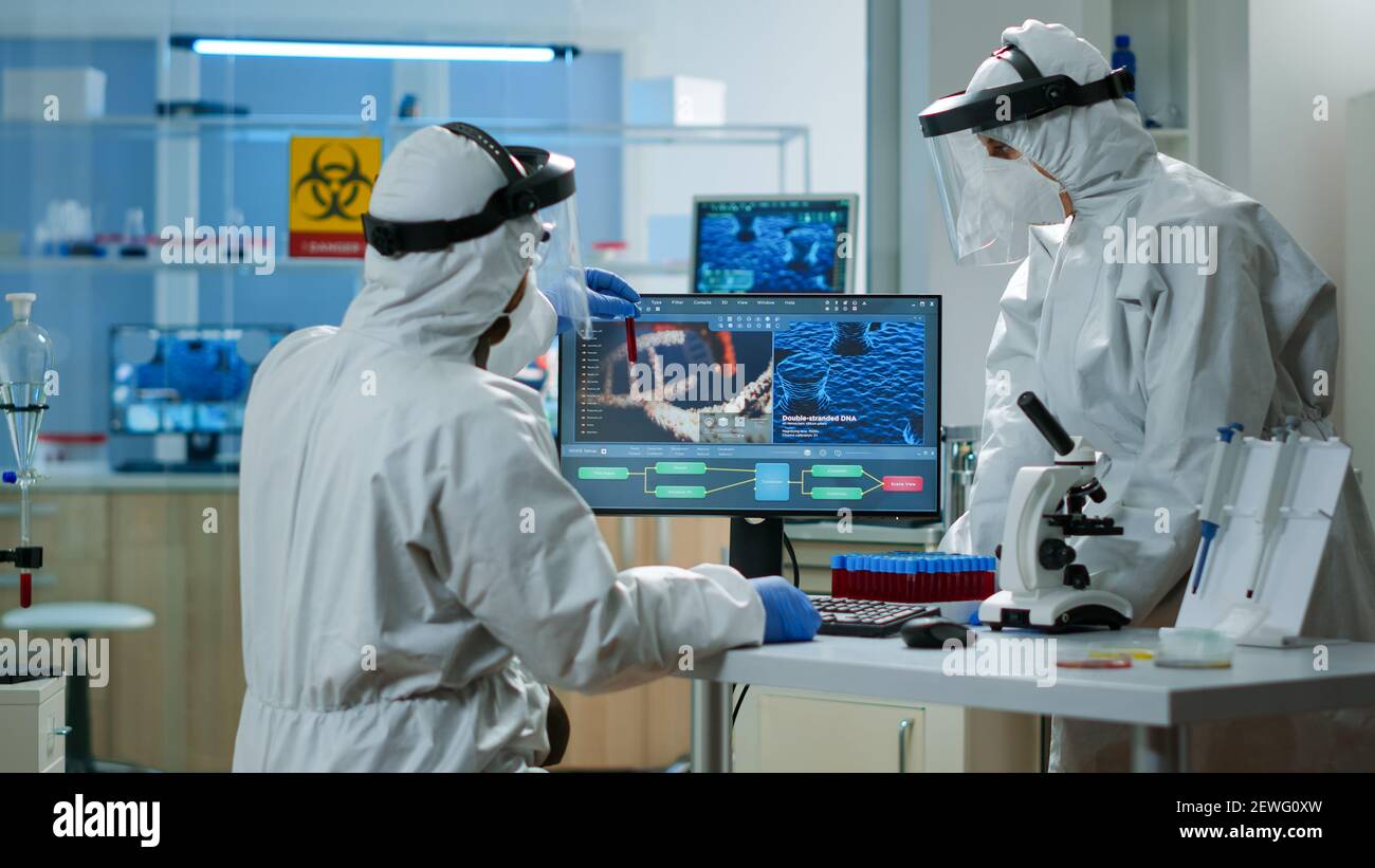 Scientists in protection suits analysing test tubes with blood sample ...