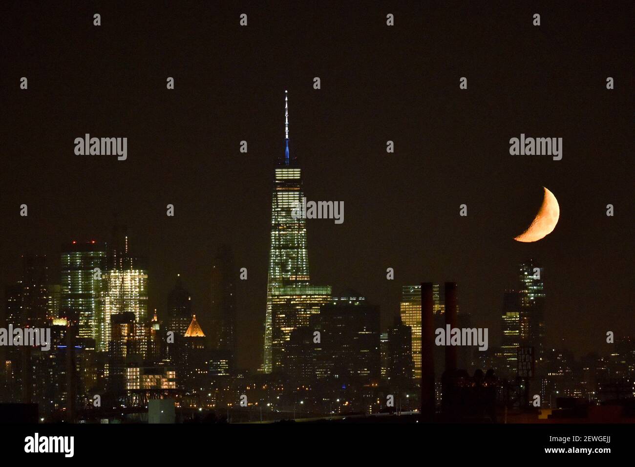 An orange waxing crescent moon (at 30 percent visibility) sets to the right of the One World