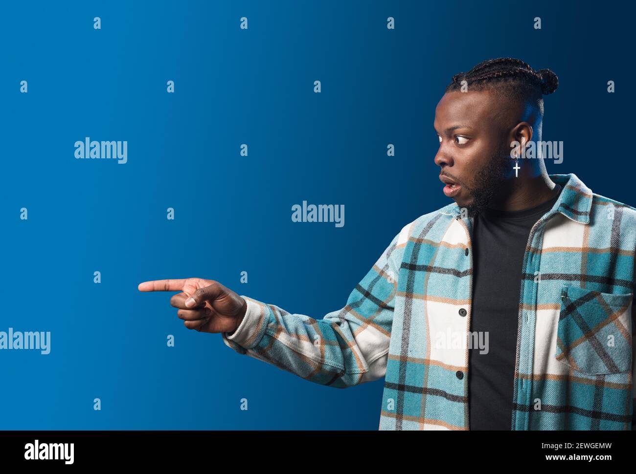 Handsome black man pointing aside, surprised. Mid shot. Blue background. Stock Photo