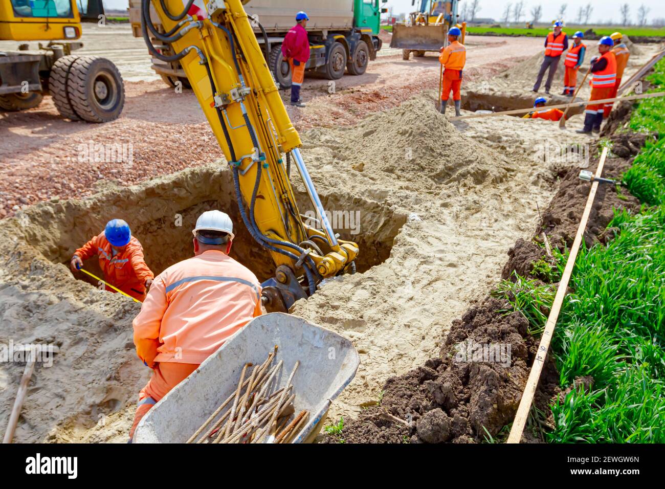 Group of workers with safety vests and helmets are help excavator to