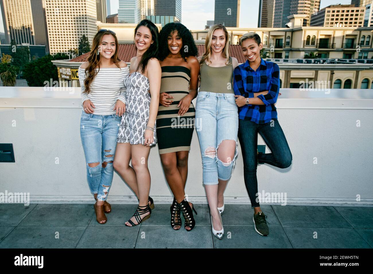 Five young women posing for photographs on a rooftop, city skyline background Stock Photo