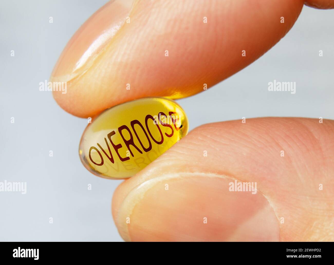 Yellow softgel pill with text overdose on it in female fingers closeup. Stock Photo