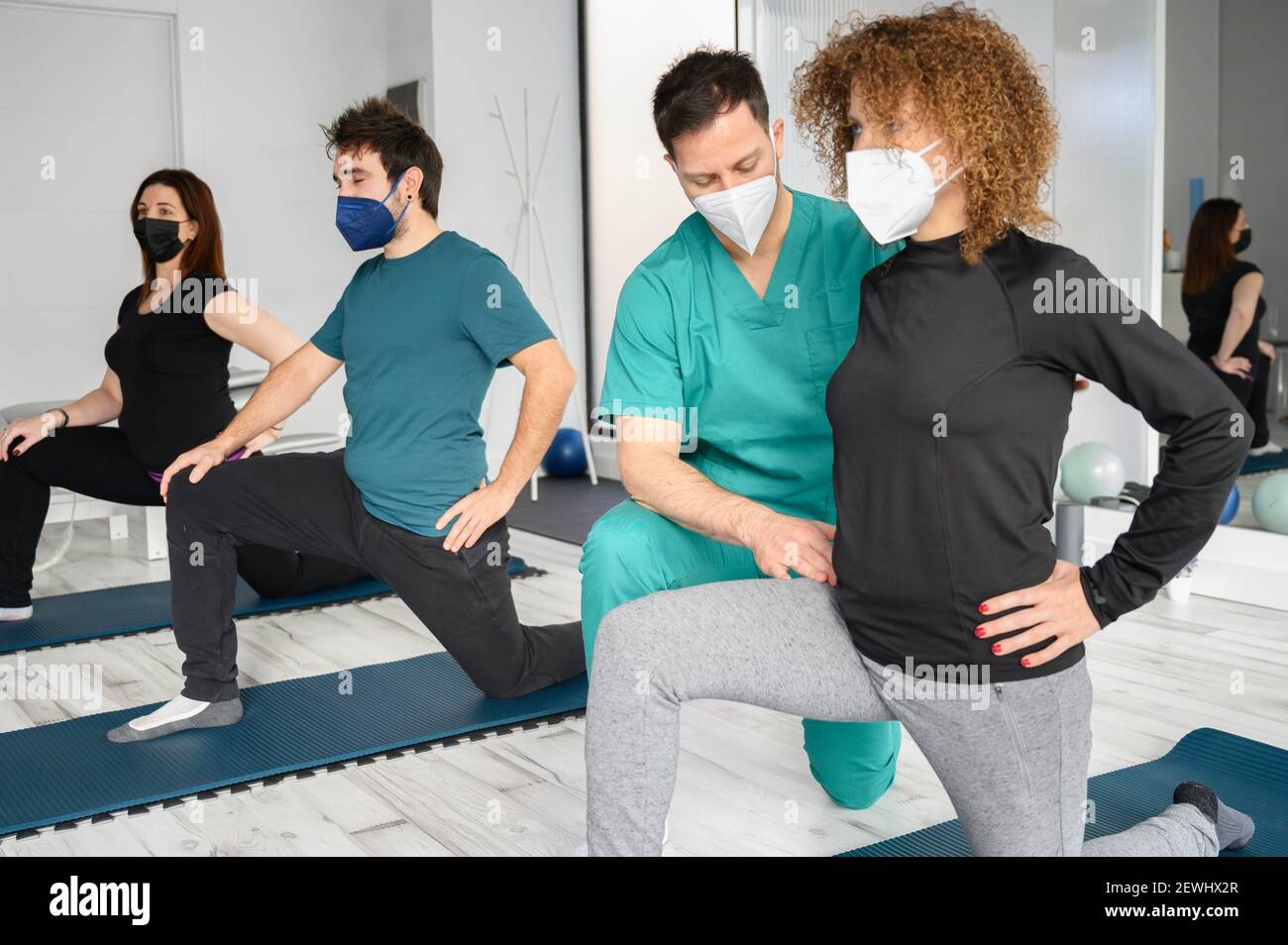 Group of persons on yoga mats assisted by physiotherapist at the rehabilitation clinic. High quality photo. Stock Photo