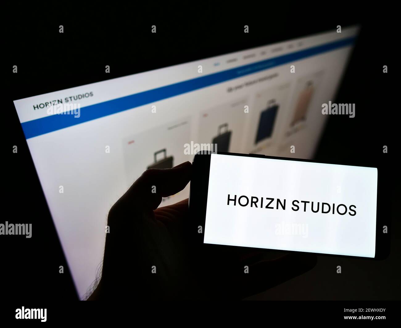 Person holding smartphone with logo of German company Horizn Studios (HS New Travel GmbH) on screen in front of website. Focus on phone display. Stock Photo