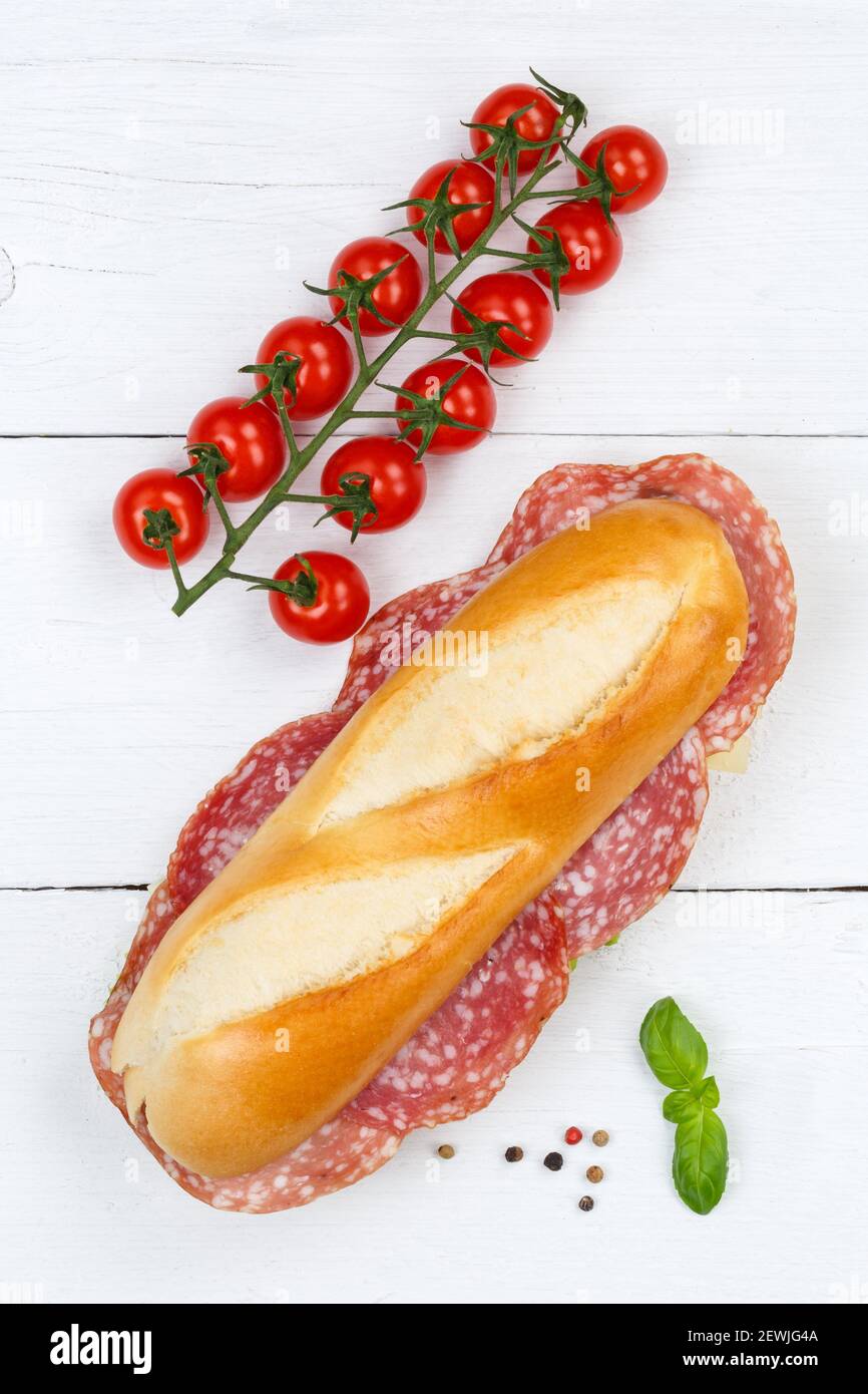 Sub sandwich baguette with salami portrait format from above on wooden board wood. Stock Photo