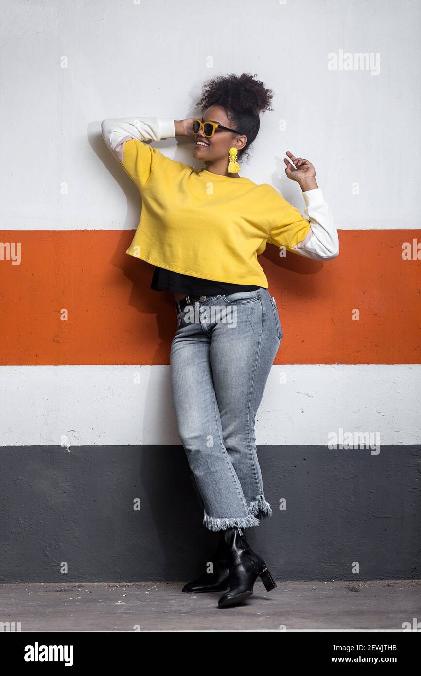 Full body of confident positive young African American female wearing trendy  jeans and bright yellow shirt with sunglasses and earrings leaning Stock  Photo - Alamy