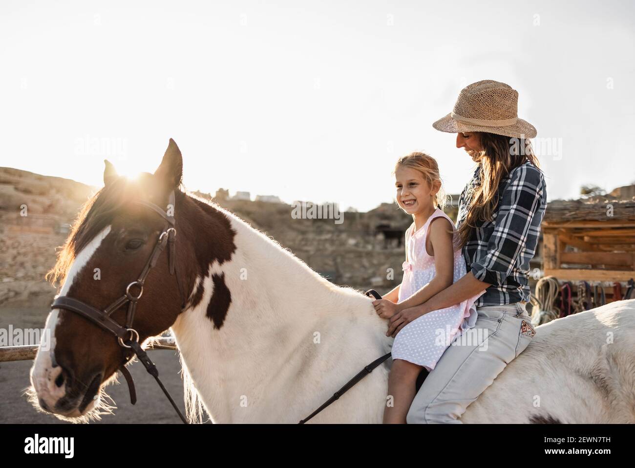 Happy mother and daughter riding a horse at sunset Main focus on