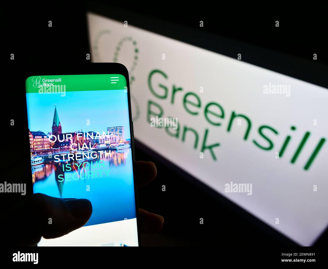 Person holding mobile phone with web page of German financial company Greensill Bank AG on screen in front of logo. Focus on center of phone display. Stock Photo