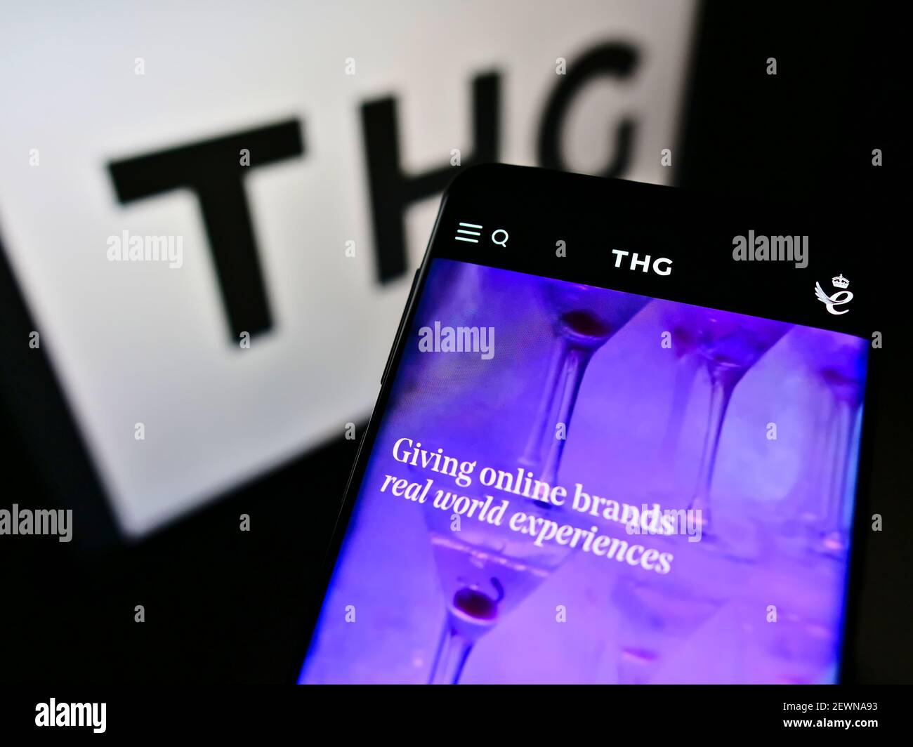 Smartphone with business website of British e-commerce company THG Holdings plc on screen in front of logo. Focus on top-center of cellphone display. Stock Photo