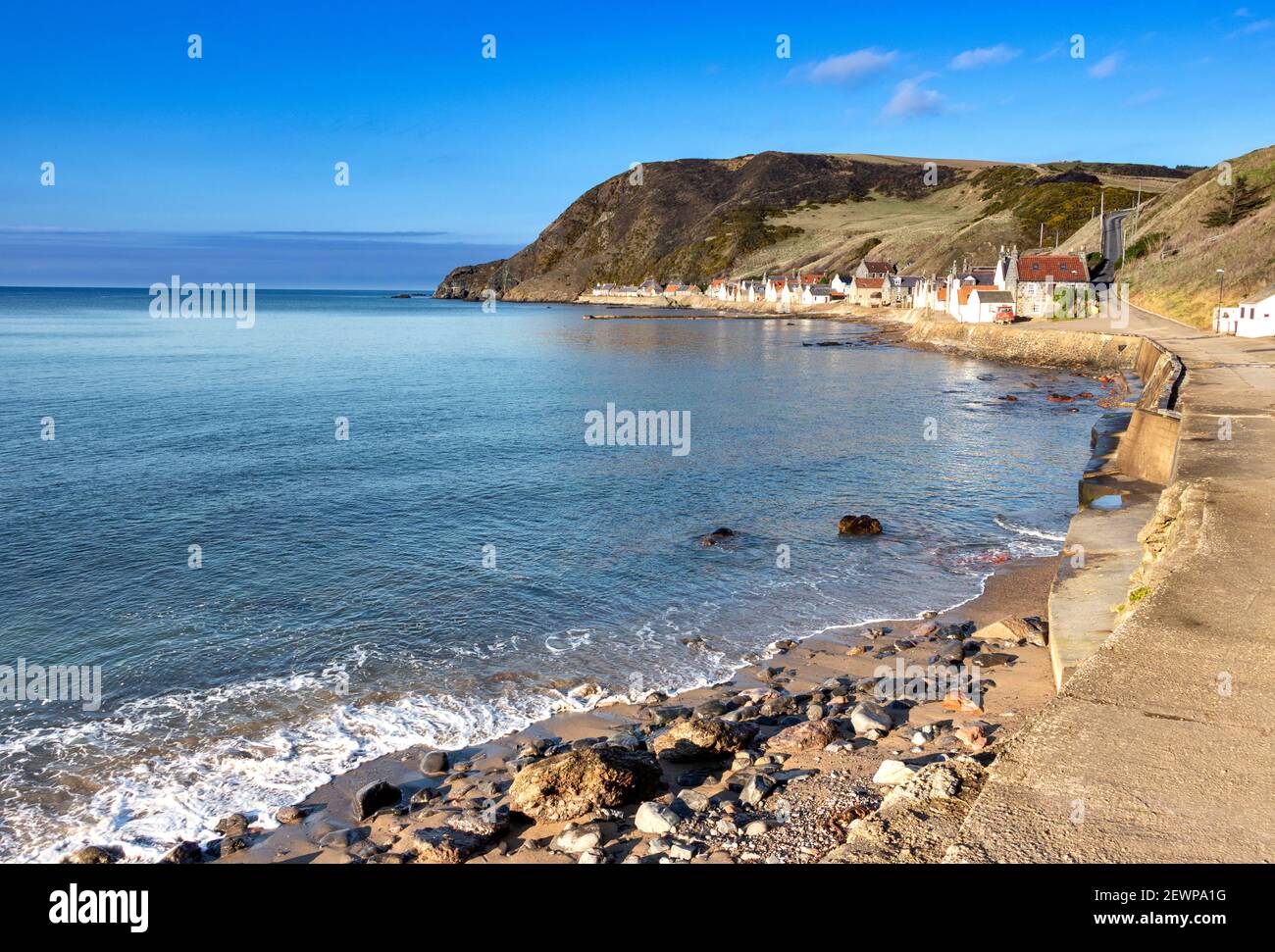 CROVIE VILLAGE ABERDEENSHIRE SCOTLAND A ROW OF HOUSES  THE WALKWAY A BLUE SKY AND A WAVE BREAKING OVER THE SAND AND PEBBLE BEACH Stock Photo