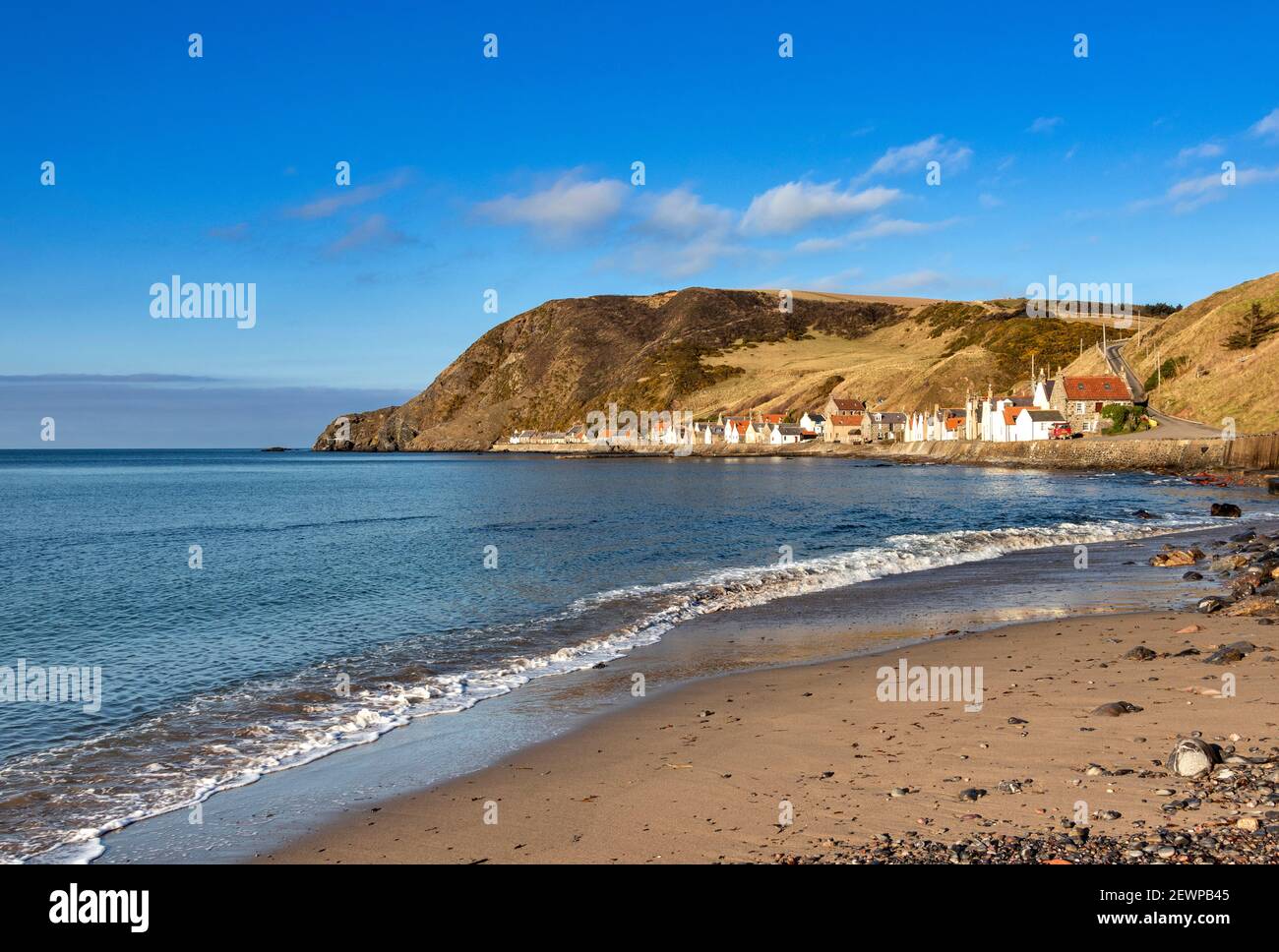 CROVIE VILLAGE ABERDEENSHIRE SCOTLAND A ROW OF HOUSES WITH RED ROOF TILES A BLUE SKY AND A WAVE BREAKING OVER A SMALL SANDY BEACH Stock Photo